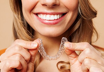 Closeup of smiling patient holding clear aligner