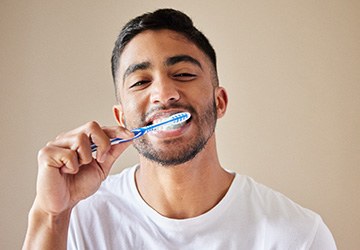 Man smiling while brushing his teeth